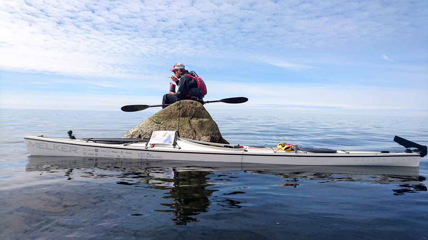 Person on a rock in the ocean with a Melker Kayak floating next to it